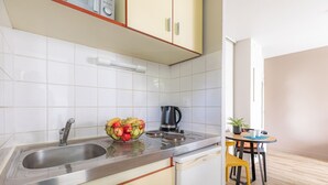 A kitchen with a stainless steel sink, a bowl of fruit, a kettle, and a small dining table with chairs. - Appart'City Classic Rennes Ouest (Rennes)