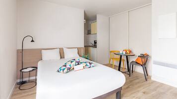 Een moderne hotelkamer met een bed, nachtkastje, lamp en een klein zithoekje met tafel en stoelen.