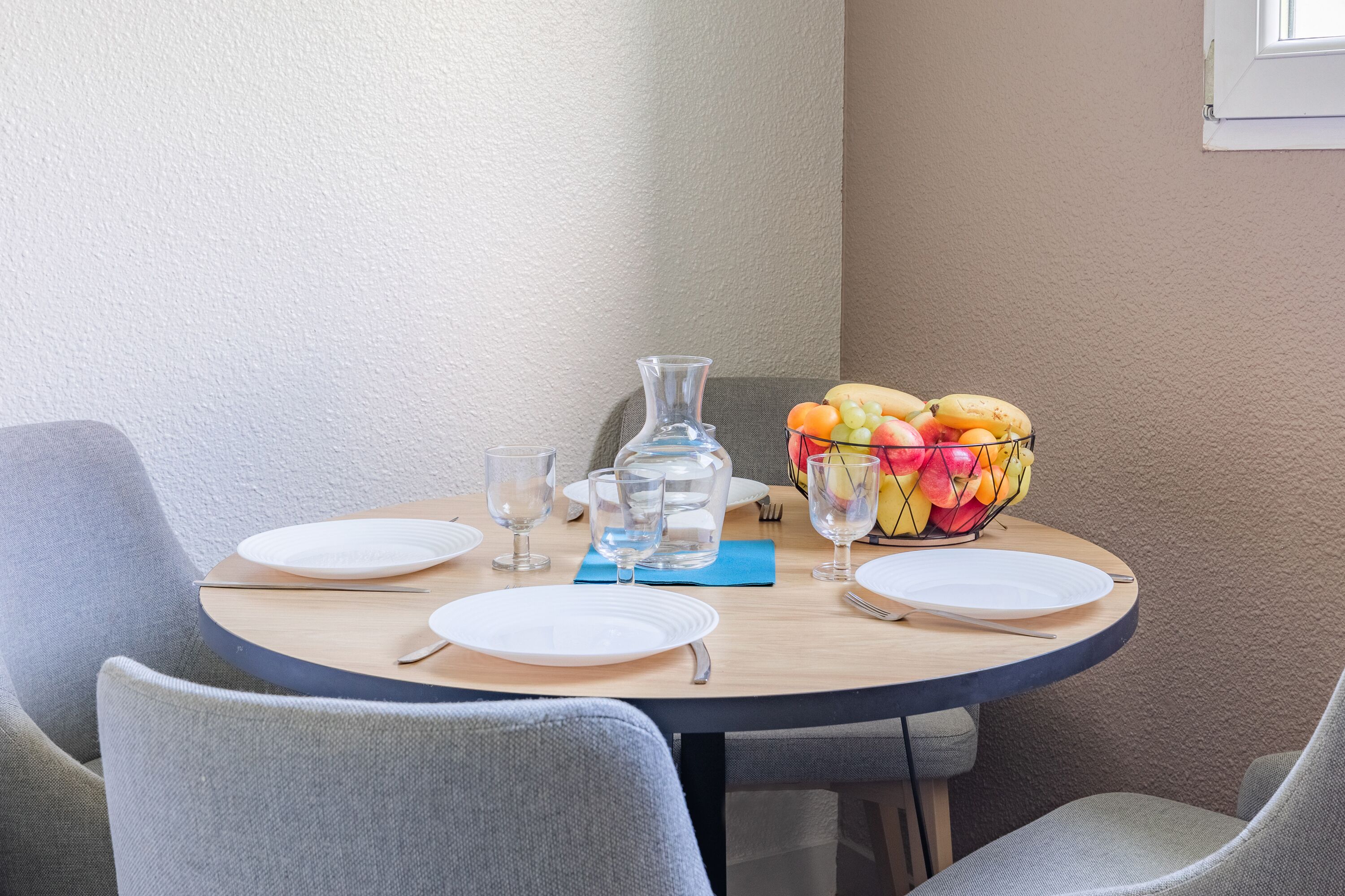 A round dining table with four plates, a pitcher, and a fruit basket.