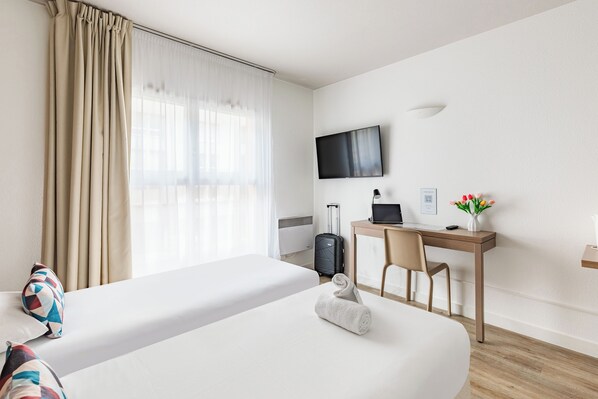 A hotel room with two beds, a desk, a chair, a TV, and a small table with a vase of flowers.