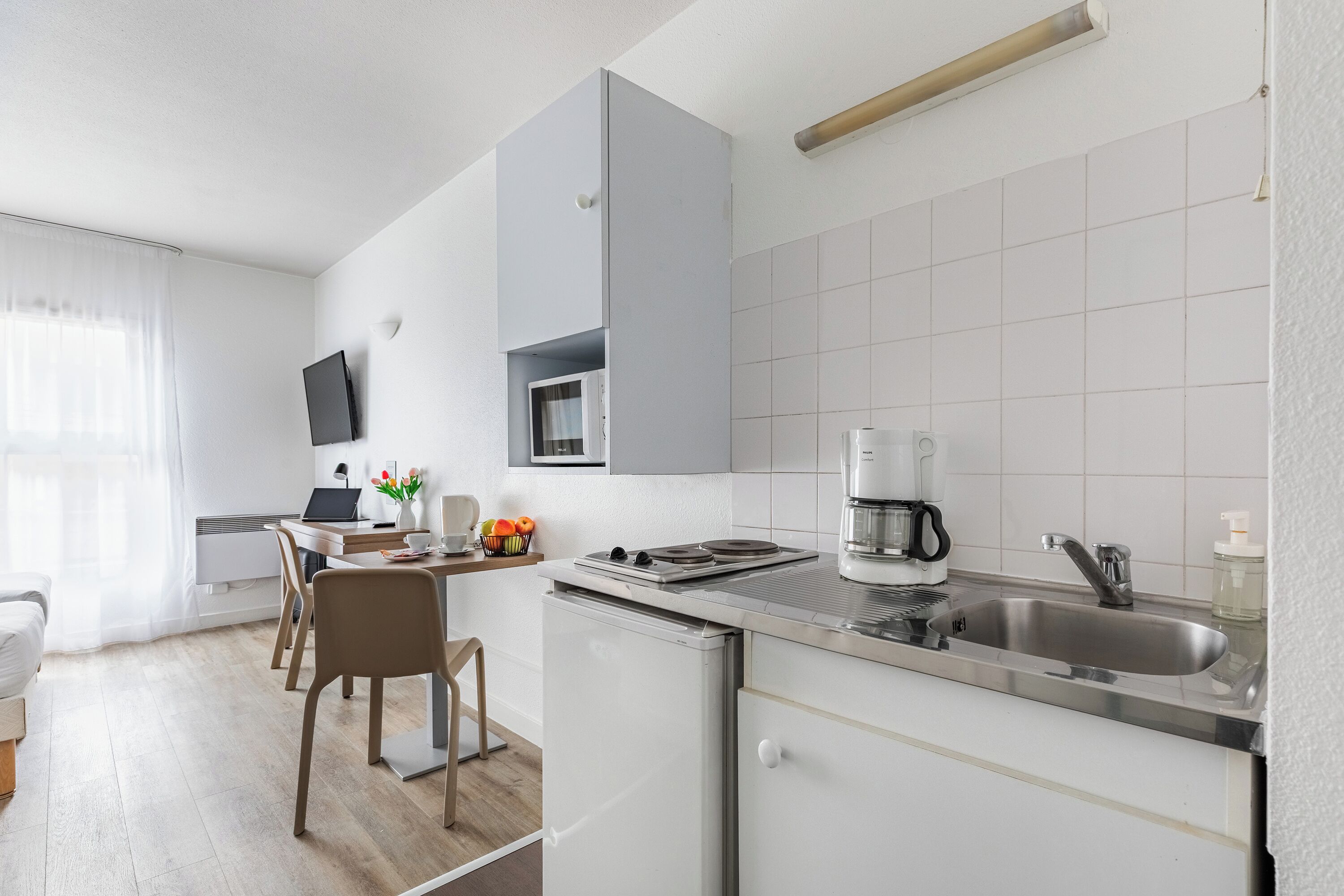 A modern kitchen with a built-in microwave, coffee maker, and sink. There is a dining area with a table and chairs.