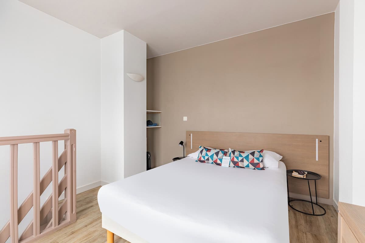 A bedroom with a bed, a nightstand, a small table, and a wooden headboard.