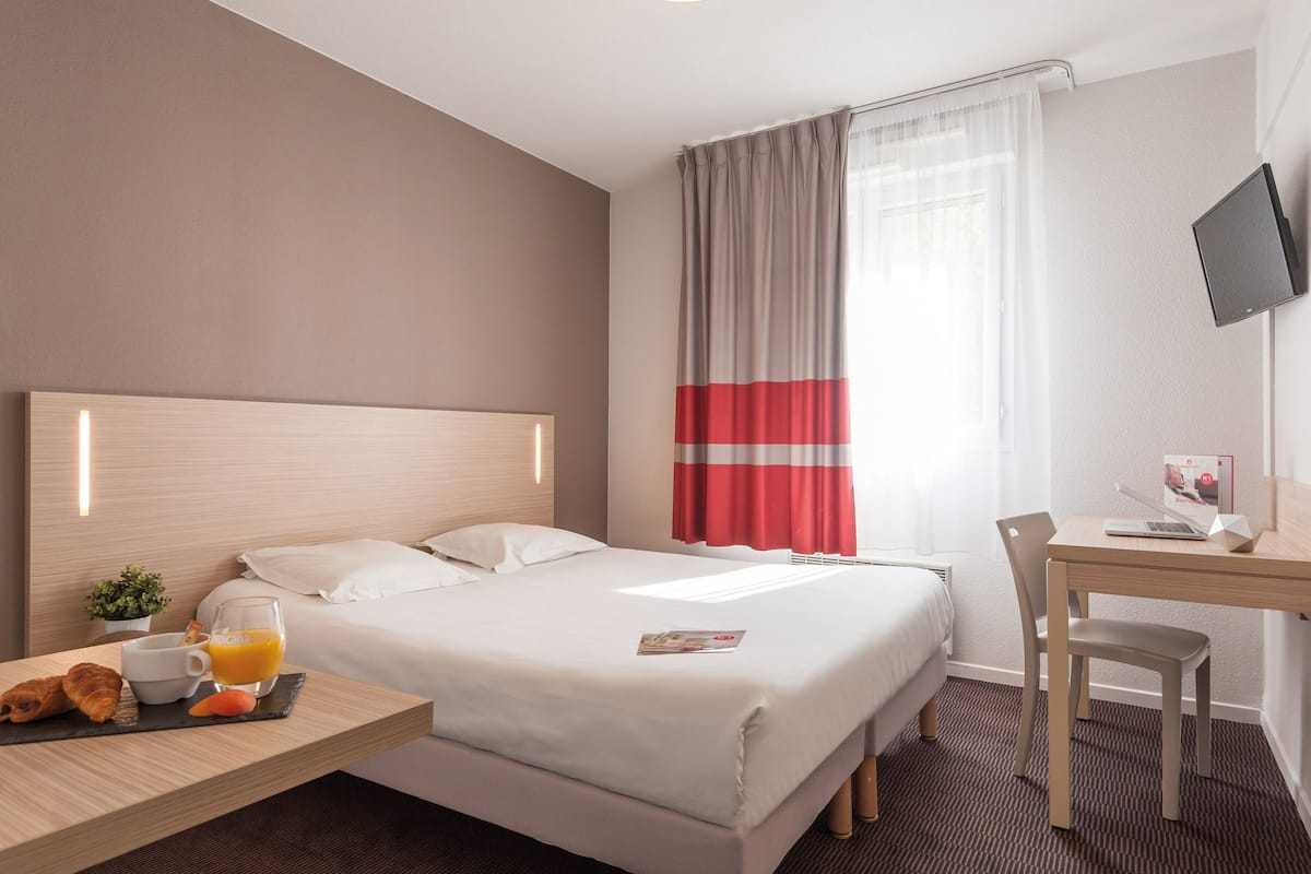 Camera d'albergo con un letto, una scrivania con una sedia, una TV e un vassoio per la colazione con cornetti e succo d'arancia.