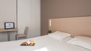 A hotel room with a bed, a desk with a laptop, a chair, and a small table with croissants and juice. - Appart'city Classic Lyon Part Dieu Garibaldi (Lyon)