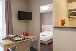 Une chambre d’hôtel comprenant un lit, un téléviseur fixé au mur, une table à manger avec des chaises et un panier de fruits.