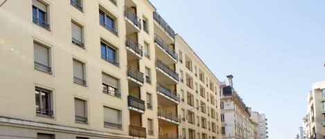 Un edificio residencial de varios pisos con balcones, autos estacionados y un cielo despejado.