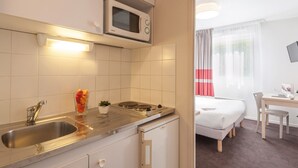 A compact kitchenette with a microwave, sink, and small stove. There's a bed and a desk in the adjacent room. - Appart'city Classic Lyon Part Dieu Garibaldi (Lyon)