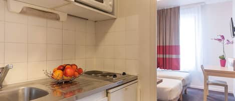 Une cuisine compacte équipée d’un four à micro-ondes, d’un évier et d’une cuisinière. On y trouve également un petit réfrigérateur, une table à manger avec une chaise, et un lit dans la pièce adjacente.