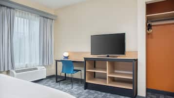 A hotel room with a bed, a desk with a television, a chair, a desk lamp, and a wardrobe.