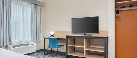Habitación de hotel con cama, escritorio con televisor, silla, lámpara de escritorio y armario.