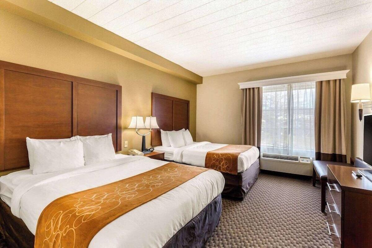 A hotel room with two beds, a desk, a chair, and a window with curtains.