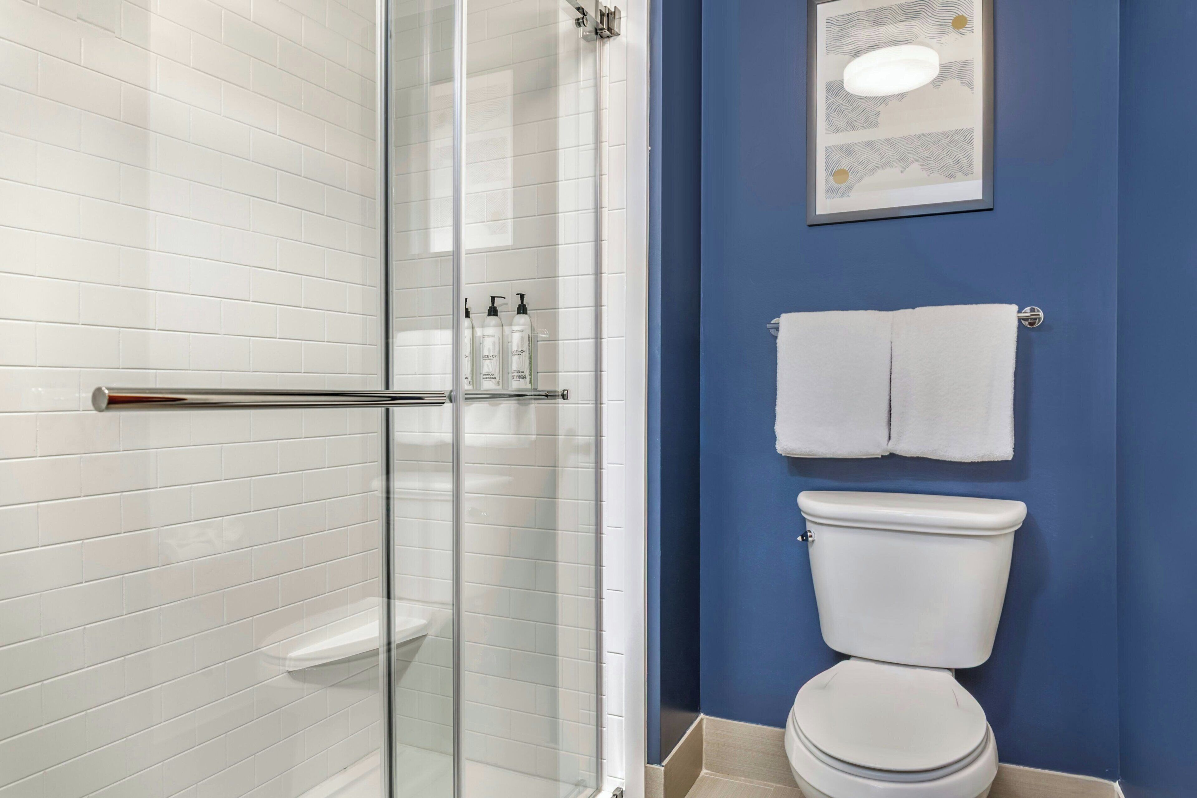 Une salle de bain avec une douche à parois de verre, des carreaux blancs, des toilettes et un mur bleu.