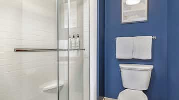 Une salle de bain avec une douche à parois de verre, des carreaux blancs, des toilettes et un mur bleu.