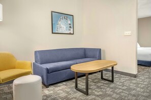 A hotel room with a blue sofa, a yellow armchair, a white ottoman, and a wooden table. - City Express By Marriott Elkridge (Elkridge)