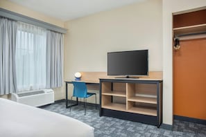 A hotel room with a bed, a desk with a television, a chair, a desk lamp, and a wardrobe.