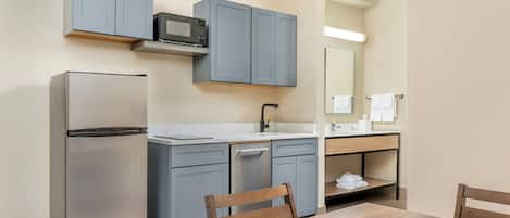 A compact kitchen with a refrigerator, microwave, sink, and a dining area with a table and chairs.