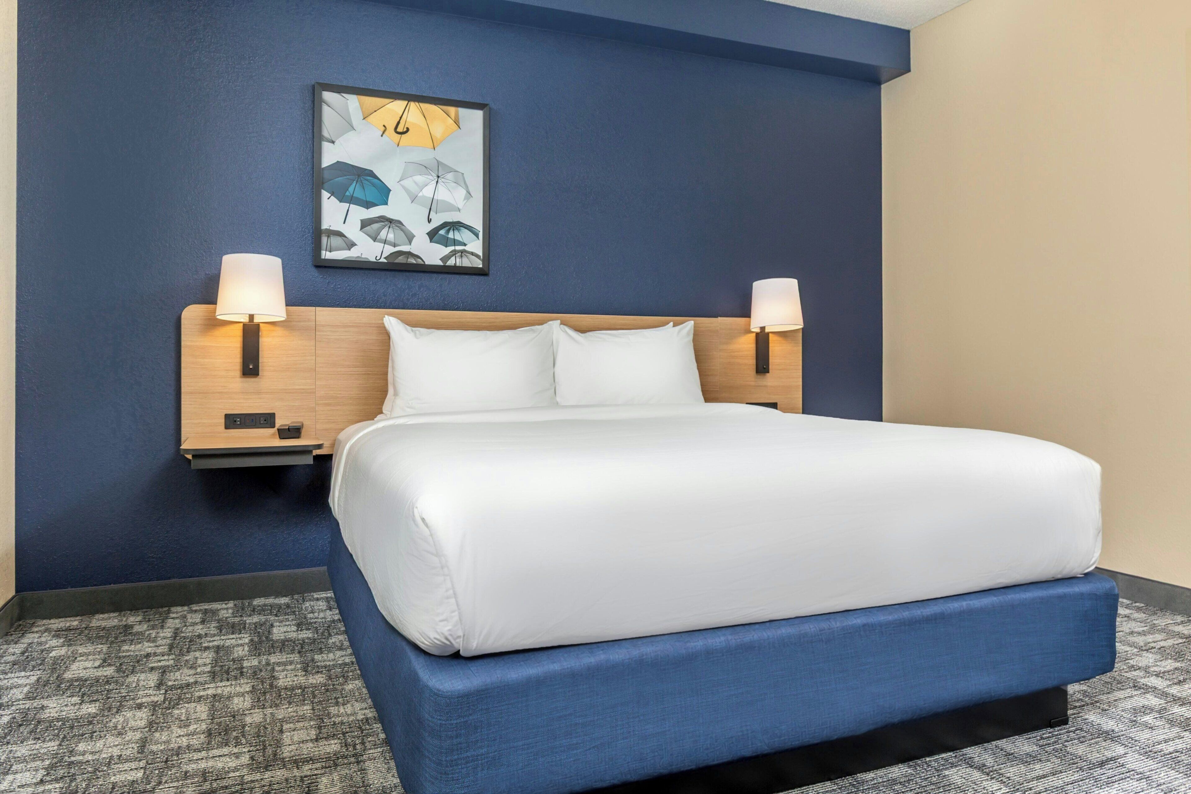 A hotel room with a large bed, two bedside lamps, a nightstand, and a wall-mounted artwork.