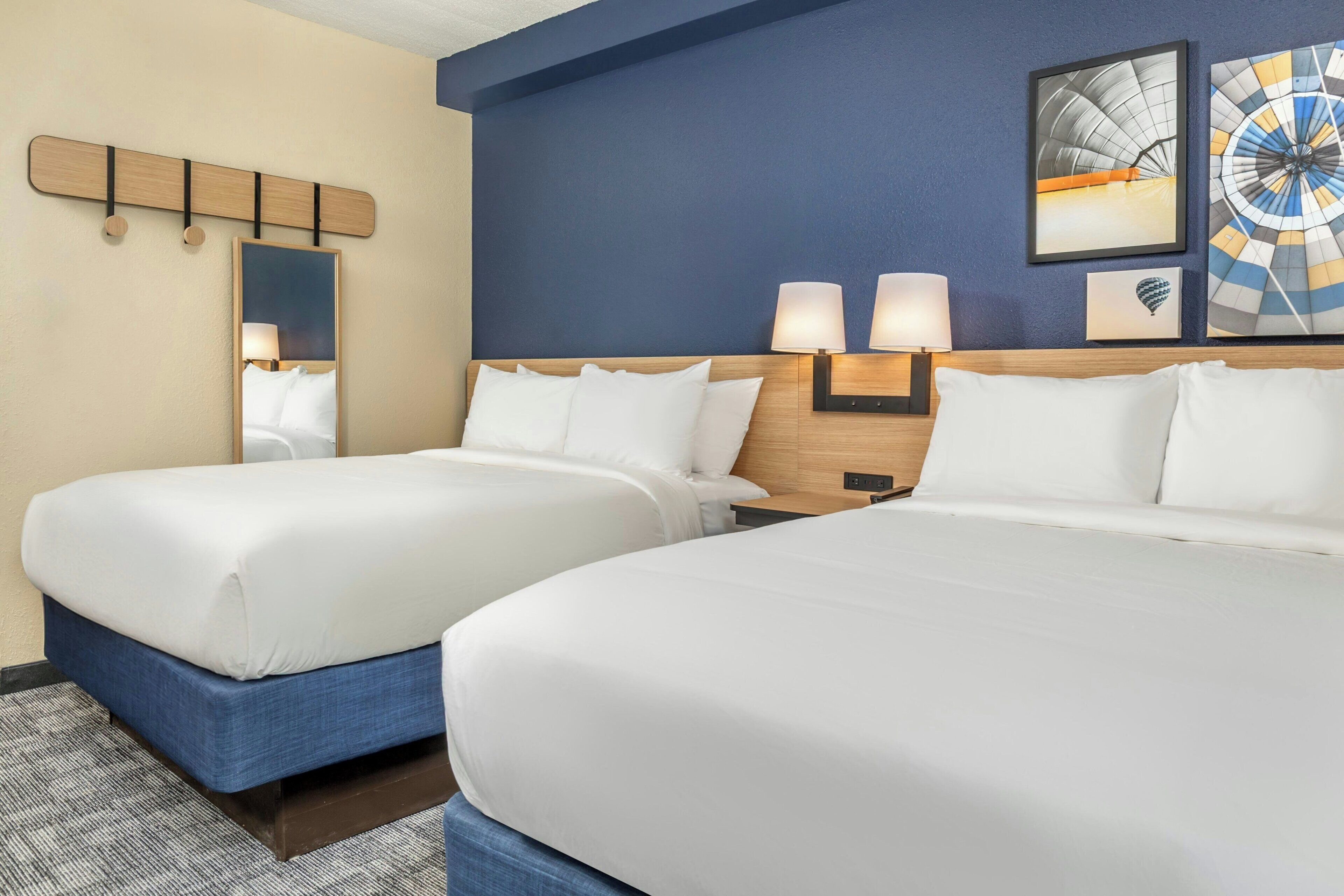 A hotel room with two beds, a large mirror, and wall-mounted lamps.