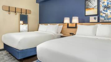 A hotel room with two beds, a large mirror, and wall-mounted lamps.