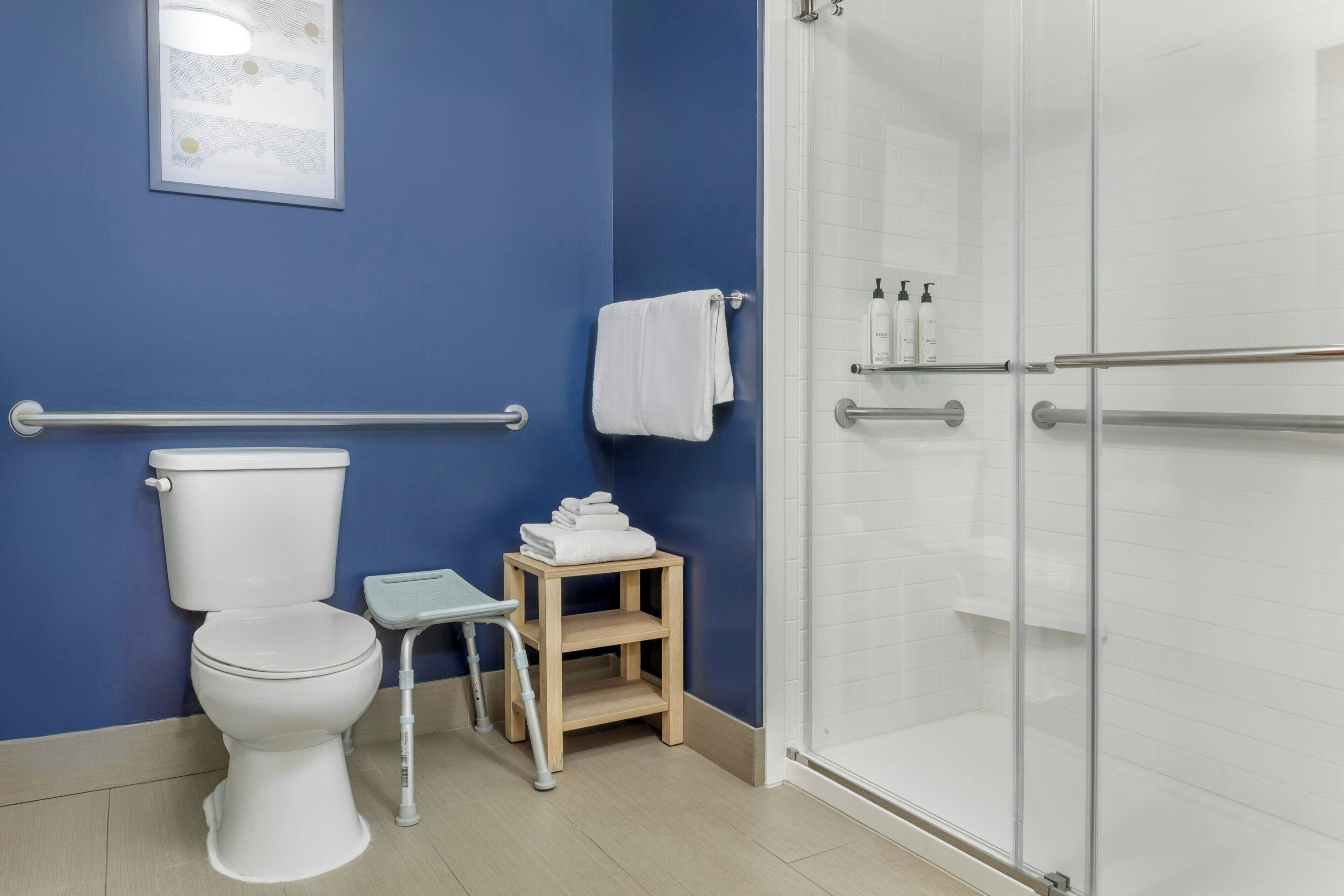 A bathroom with a toilet, a small wooden stool, a glass shower enclosure, and a towel rack.