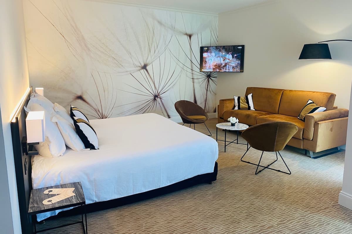 Une chambre d’hôtel avec un lit, un canapé, une petite table et un téléviseur fixé au mur.