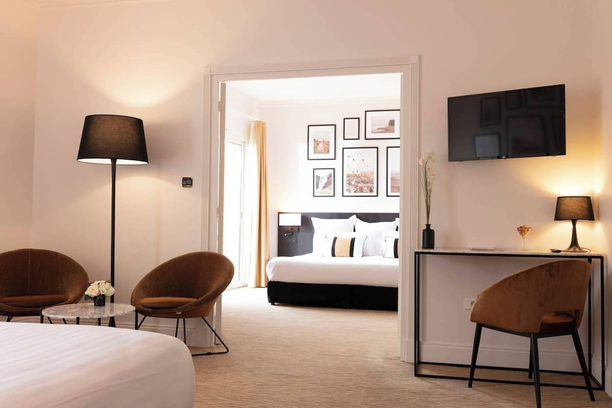 Une chambre d’hôtel comprenant un lit, deux fauteuils, un bureau avec une lampe, une télévision et des tableaux encadrés accrochés au mur.