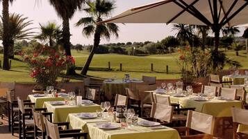Een terras met tafels gedekt voor gasten, omringd door palmbomen en uitzicht op een golfbaan.