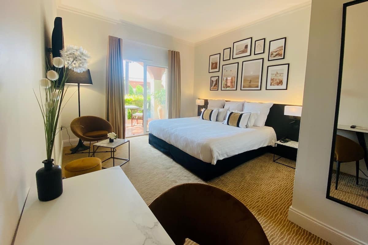 Une chambre d’hôtel avec un lit, un bureau, une chaise, une lampe et une vue sur l’extérieur.