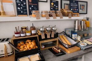 Un buffet de petit-déjeuner proposant une variété d’aliments, notamment des viennoiseries, du pain et des condiments.