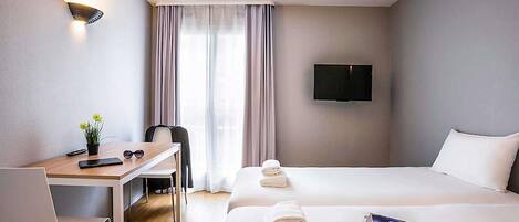 A hotel room with a desk, two beds, a TV, and a window with curtains.