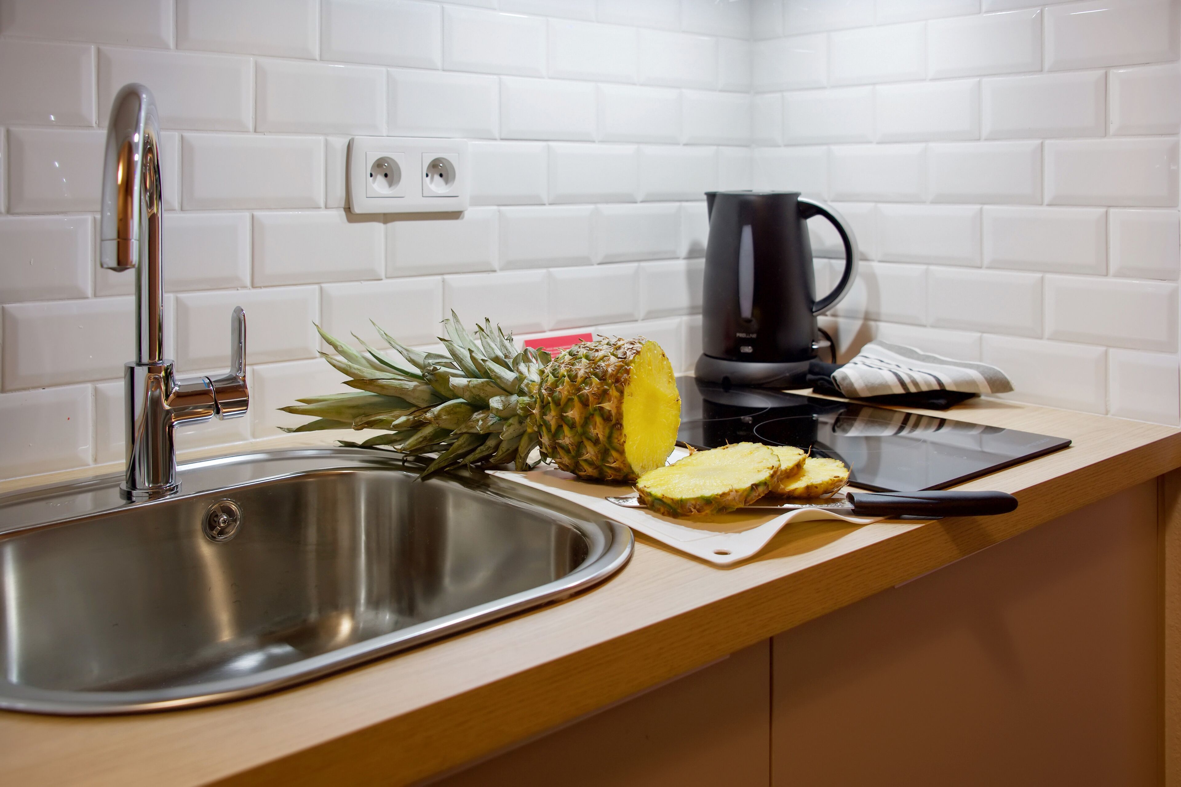 Une cuisine avec un évier en acier inoxydable, une machine à café noire, un ananas et une planche à découper.