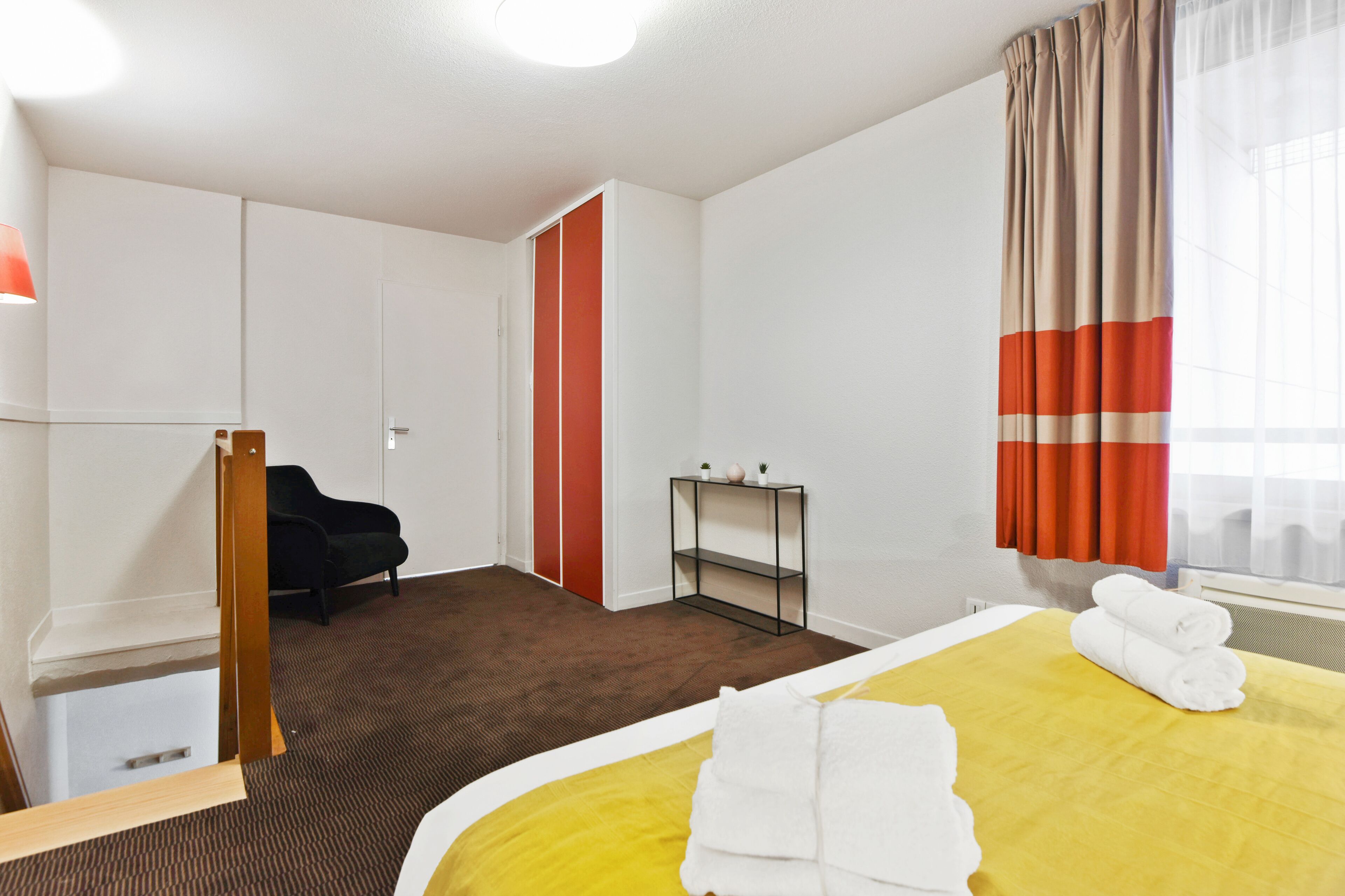 A hotel room with a bed, a desk, a chair, a wardrobe, and a window with curtains.
