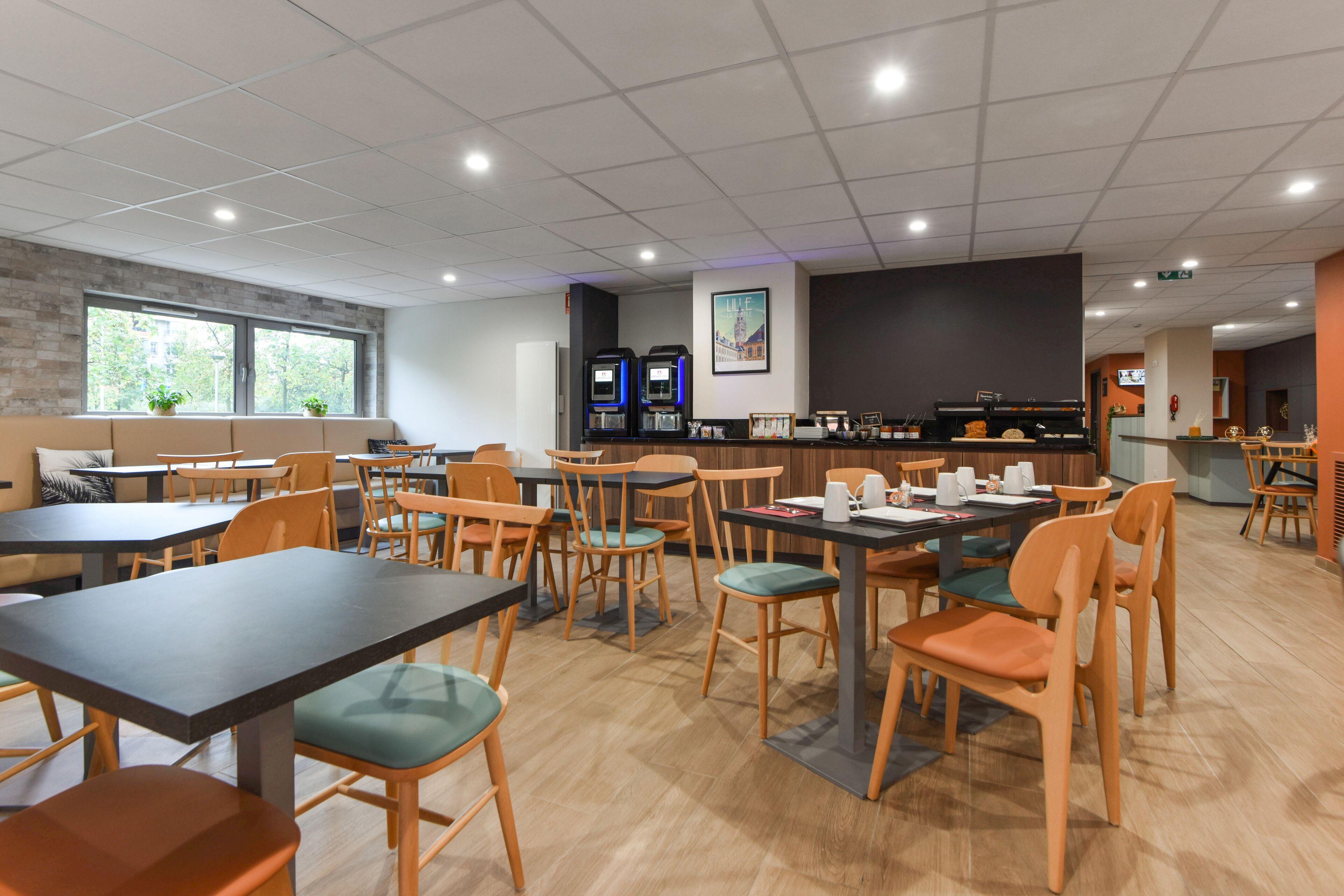 Uma sala de jantar moderna com várias mesas e cadeiras, um balcão com uma máquina de café e uma janela grande com plantas.