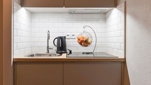 Une petite cuisine équipée d’un évier, d’une bouilloire et d’un panier de fruits.