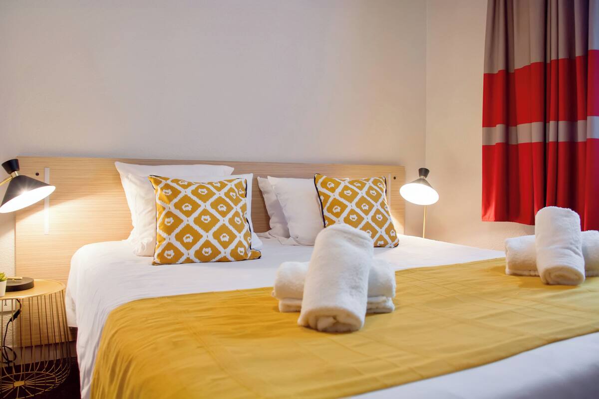 Un lit bien fait, avec une couvre-lit jaune, des oreillers blancs et une tête de lit.