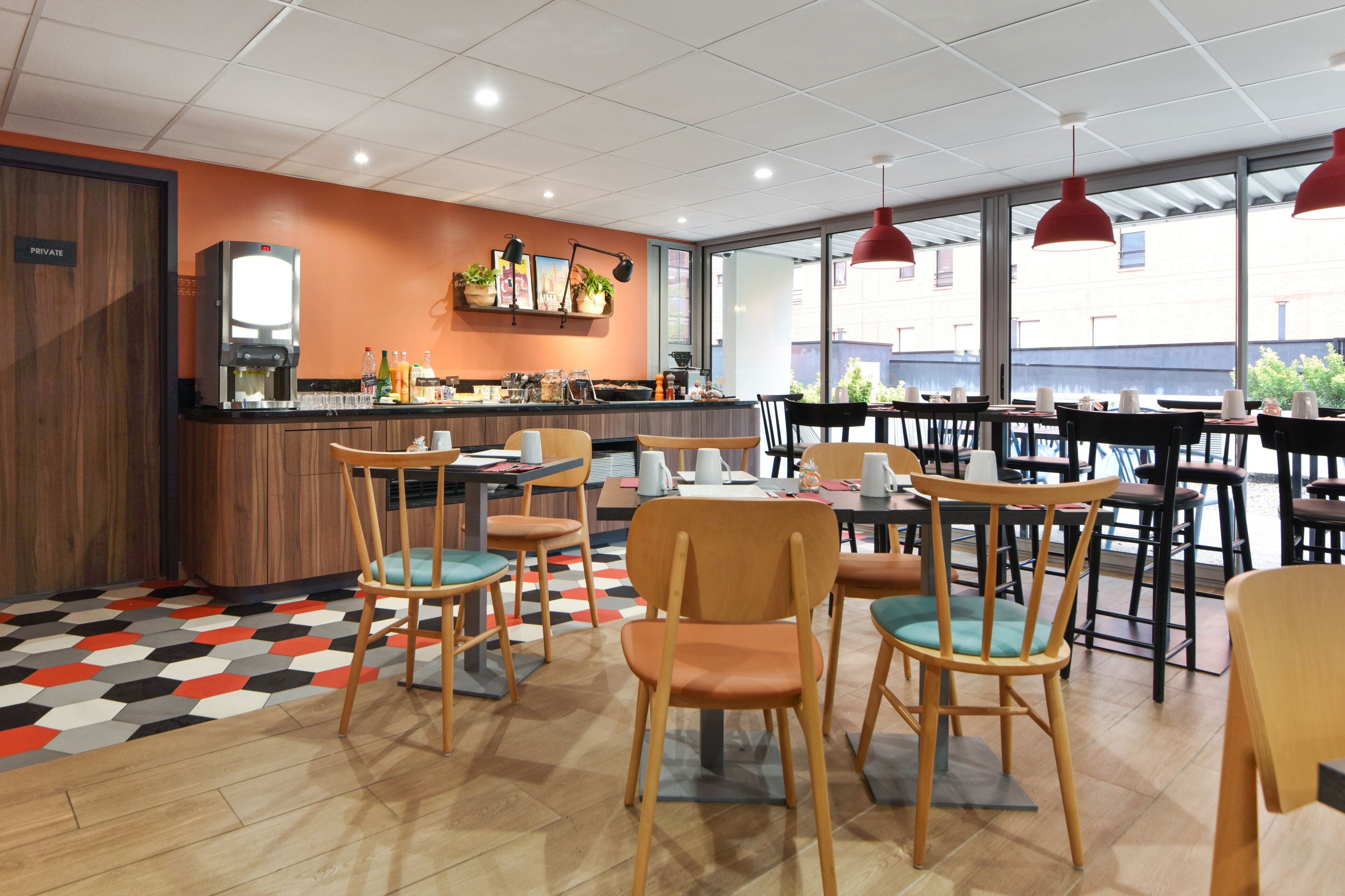 A modern cafe with wooden chairs and tables, a coffee machine, and a counter with various items.