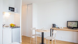 A modern kitchen with a microwave, sink, and a dining area with two chairs and a table. - Comfort Aparthotel Le Mans (Le Mans)
