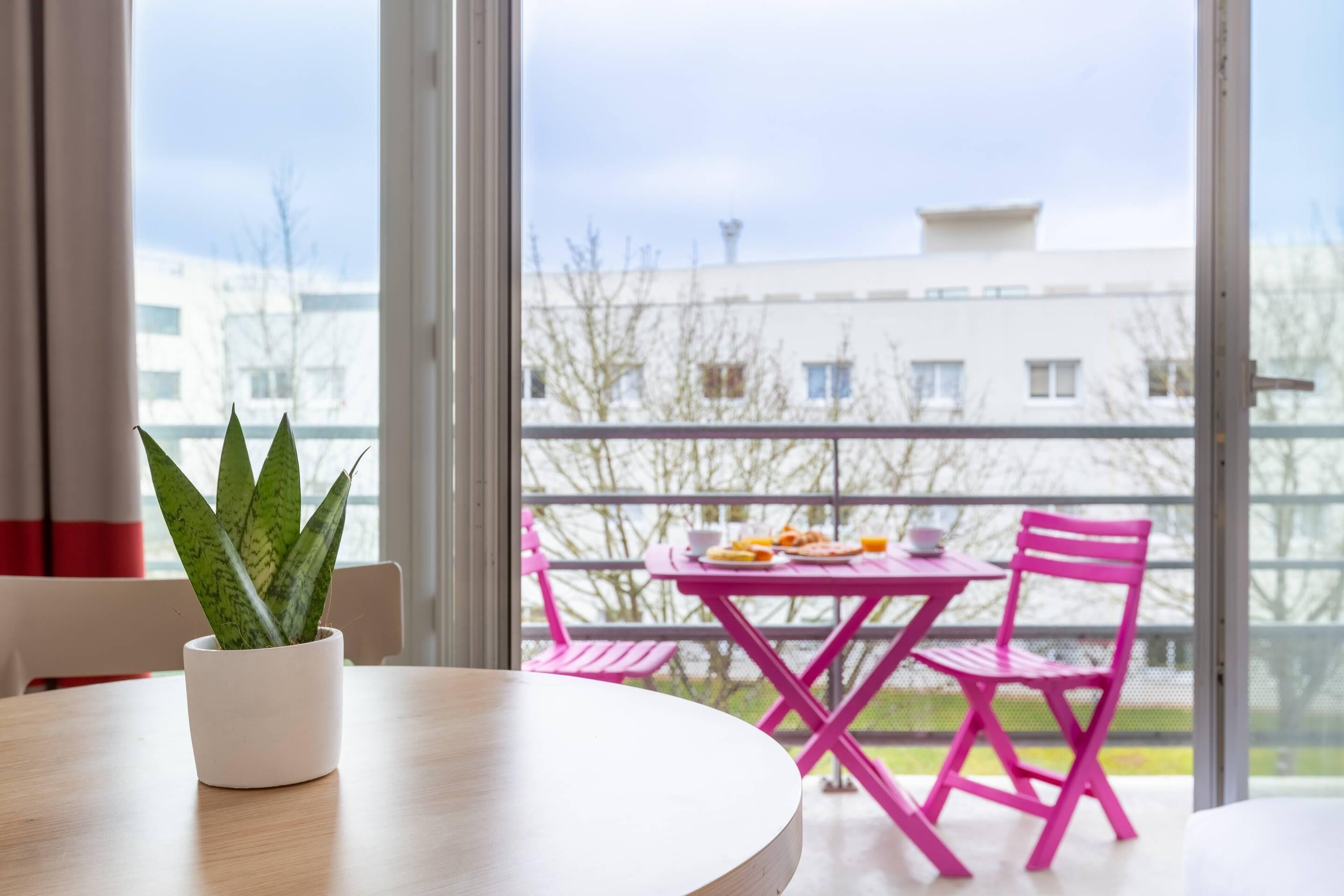 A balcony with a table and chairs, a potted plant, and a view of buildings.
