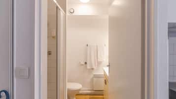 A narrow hallway leading to a bathroom with a toilet, a shower, and a towel rack.
