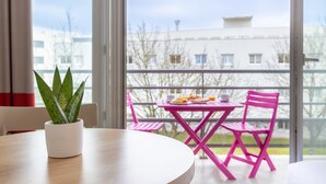 A balcony with a table and chairs, a potted plant, and a view of buildings. - Comfort Aparthotel Le Mans (Le Mans)