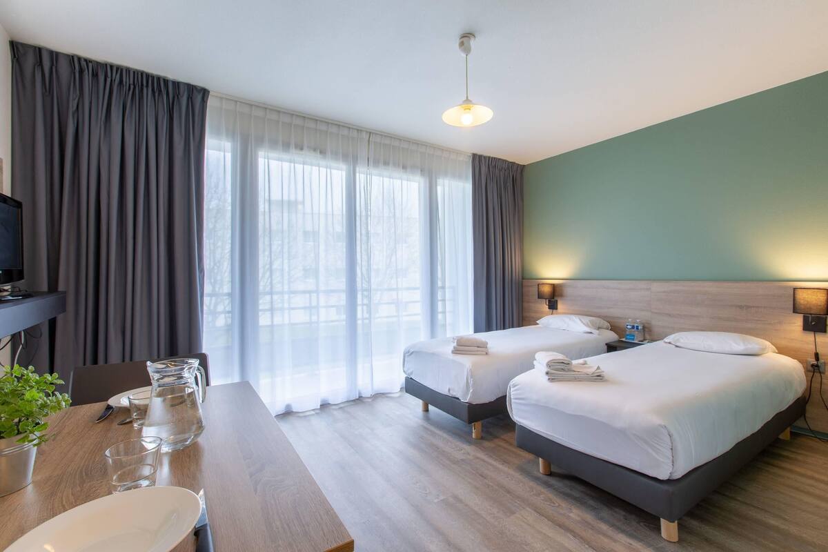 A hotel room with two beds, a wooden desk with a pitcher of water, and a TV.