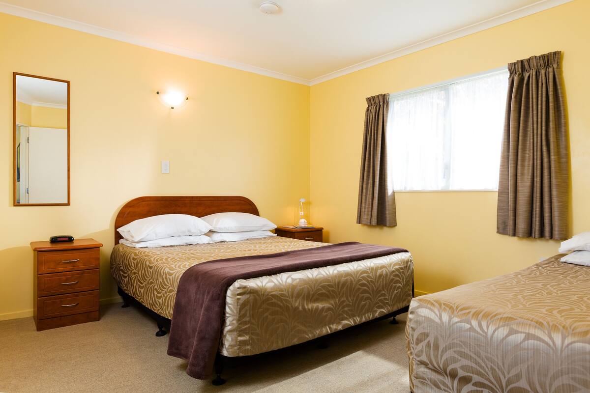 Hotelkamer met een bed, nachtkastje, spiegel en raam met gordijnen.