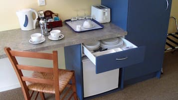 Eine kleine Küchenzeile mit einer Mikrowelle, einem Toaster und einem kleinen Kühlschrank. Ein Holzbstuhl und ein Tablett mit Tassen und einer Kaffeekanne stehen bereit.