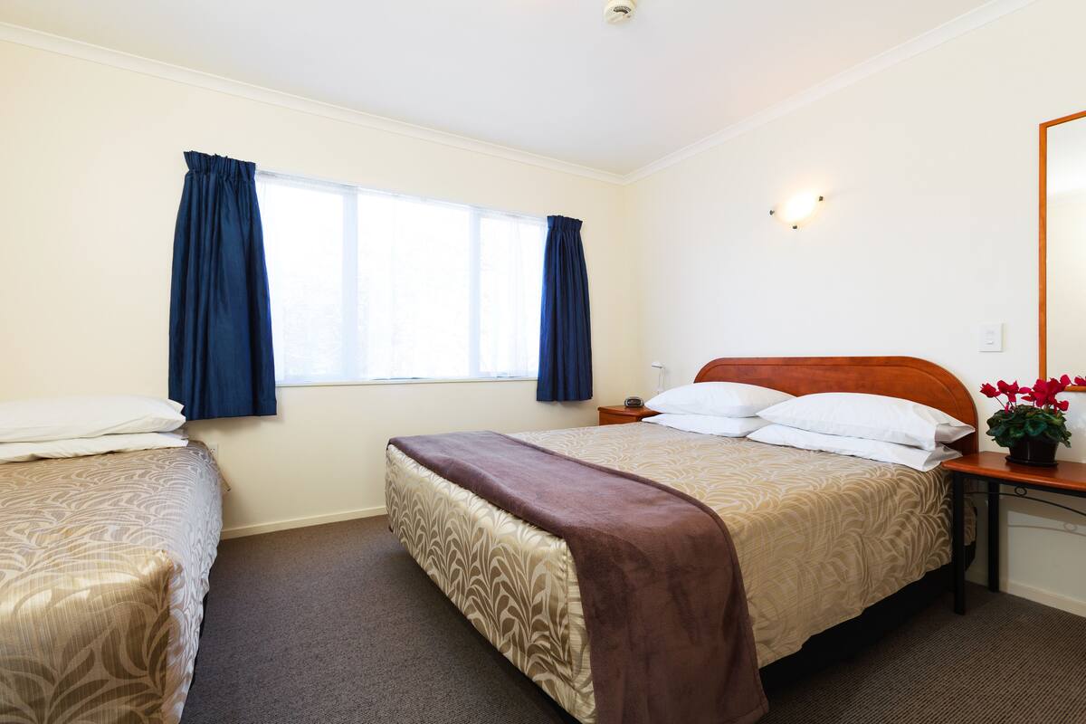Een hotelkamer met twee bedden, een nachtkastje, een spiegel en een raam met gordijnen.