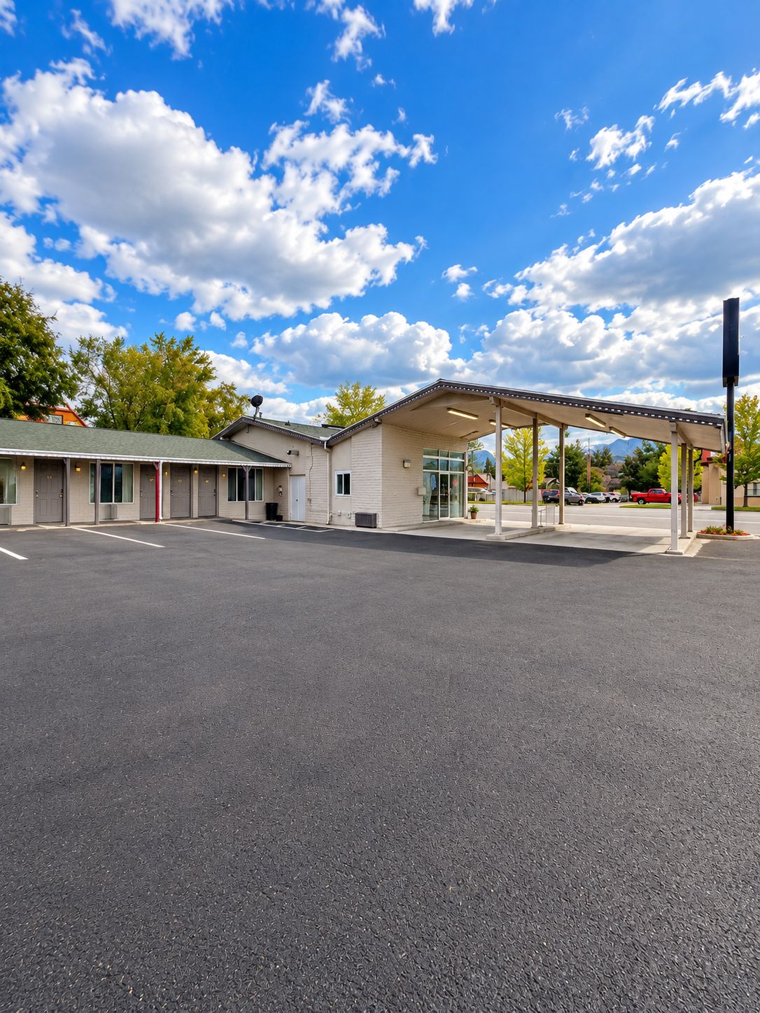Un motel con zona de estacionamiento techada, un edificio de una sola planta y cielo despejado.