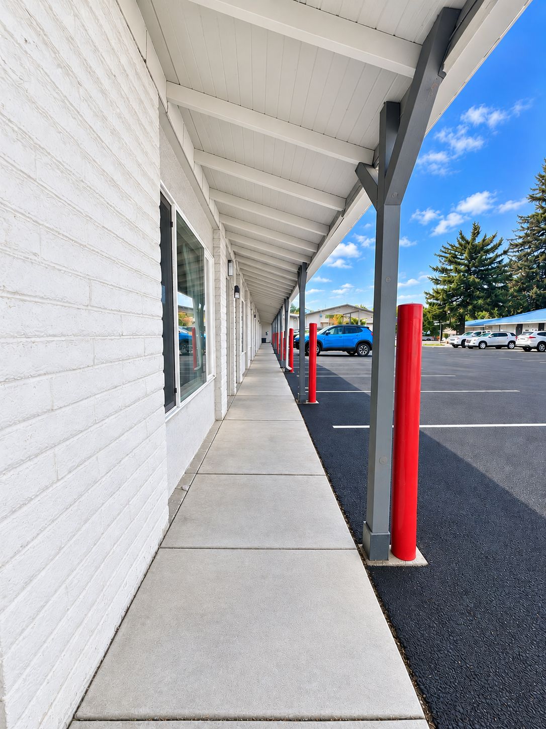A covered walkway with a white building on one side and a parking lot with cars on the other.