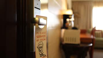 Eine Hotelzimmertür mit einem Schild, das zur Zimmerreinigung auffordert, sowie eine Lampe, ein Tisch und ein Stuhl im Hintergrund.