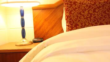 A neatly made bed with white linens, a wooden nightstand with a lamp, and a patterned pillow.
