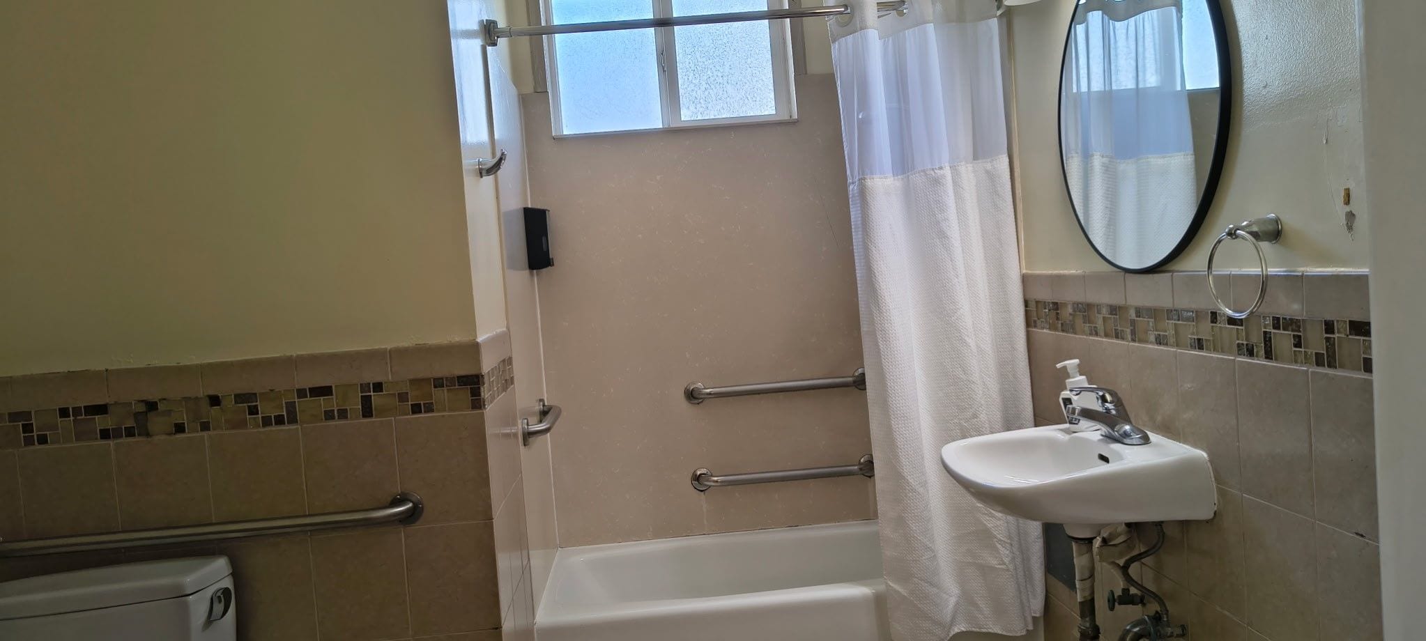Een badkamer met een bad, douchegordijn, wastafel met spiegel en een handgreep.