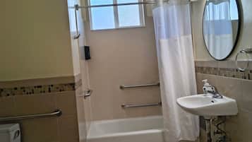 A bathroom with a bathtub, a shower curtain, a sink with a mirror, and a handrail.